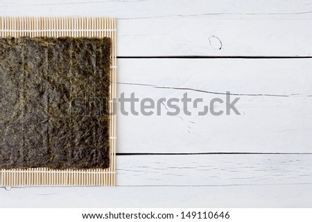 A sheet of dried seaweed Nori on a makisu mat on a white aged table with copy space