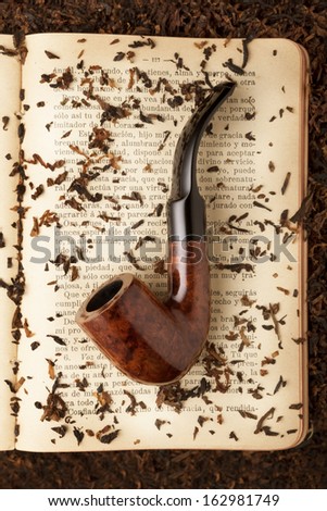 Smoking curve pipe on a open book with some tobacco scattered around them