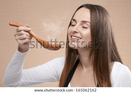 Female cook smells a steaming wooden spoon that holds in front of her face with her eyes closed. Close up