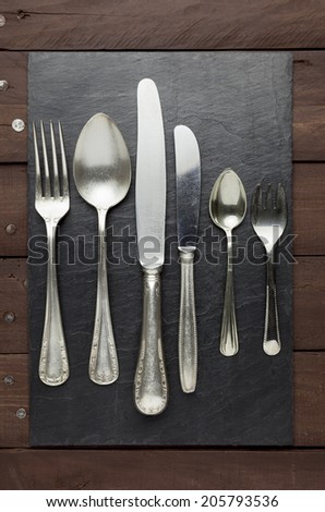 Well-worn cutlery on a square shaped slate on a brown wooden table.
