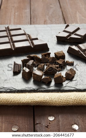 Pieces from a square of chocolate on a slate plate, on a brown wooden table. Vertical composition