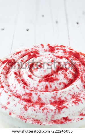 Extreme close up of a circular red velvet cake on a golden plate and on a white wooden table. The top side of cake has a spiral shape as decoration. High angle view.