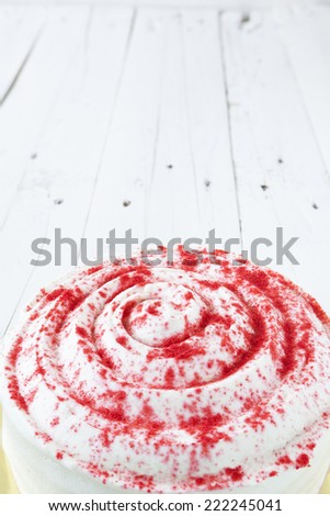 Close up of a circular red velvet cake on a golden plate and on a white wooden table. The top side of cake has a spiral shape as decoration. High angle view.