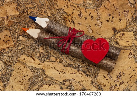 Photography with a gift on Valentine\'s Day. Textile red heart, two wooden pencil related red cord on a cork background. Can be used as greeting card for Valentine\'s day.