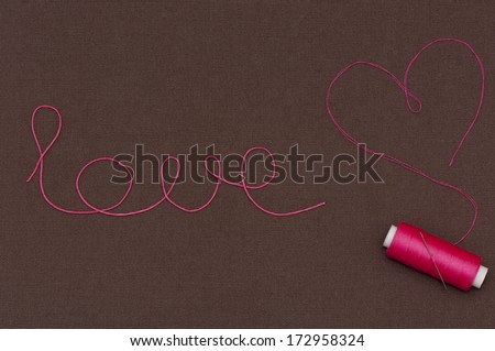 Love heart and pink thread. Pink reel of thread, needle and thread of a heart on a brown cotton fabric. Postcard, background on Valentine\'s Day.