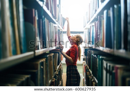 Woman taking book from library bookshelf. Young librarian searching books and taking one book from library bookshelf