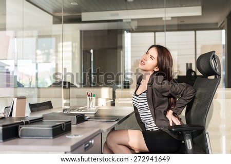 Young businesswoman having back pain while sitting at office desk