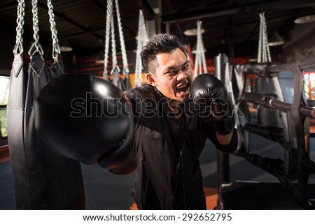young aggressive businessman training shadow boxing at gym with gloves throwing vicious punch in angry rage face expression. fighting business concept.