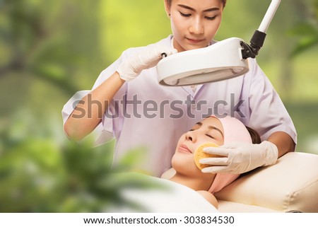 Young beautiful woman receiving cosmetic facial mask in spa beauty salon and relax. In background tropical plants
