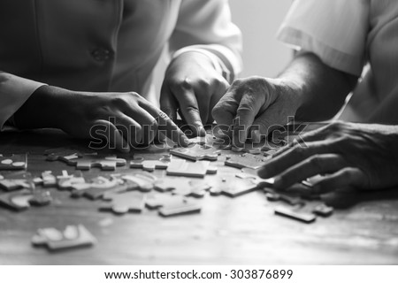 Elder care nurse playing jigsaw puzzle with senior man in nursing home. black and white