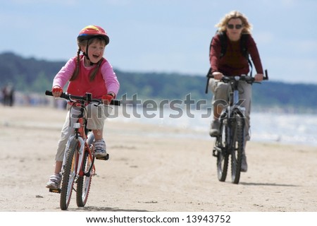 Mother and daughter riding with bicycles along the beach