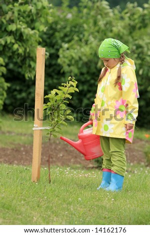 Little girl watering apple tree with watering can