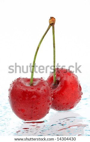 Two red cherries with water droplets over white background