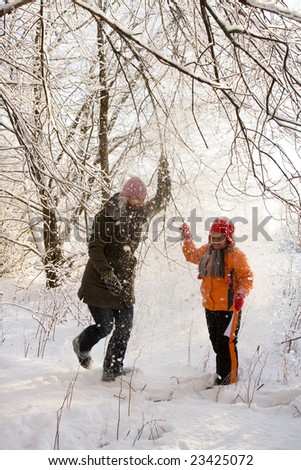 Mother and daughter walking in forest, evening sun and snow falling from trees