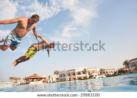 Two men jumping in swimming pool. Low angle view from the swimming pool.