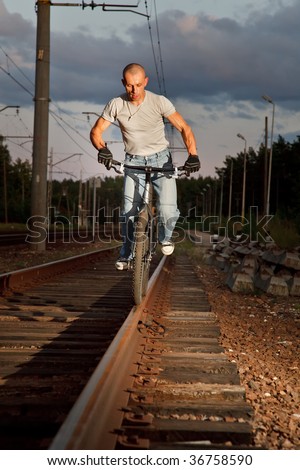 Freestyle young man riding with bicycle on railways rail. Low angle view with selected lighting.