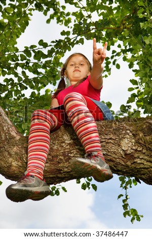 Little girl climbed on tree and sitting on tree branch, low angle view