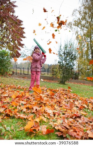 Little girl rake colorful fallen autumn leaves in garden and having fun
