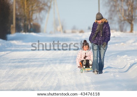 Mother pulling daughter on sledge, bright and white winter scene
