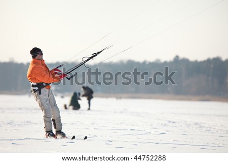 Kiteboarding on skis on the frozen river, people fishing in background