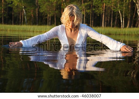 Woman swimming in dark forest lake, nice reflection from water surface