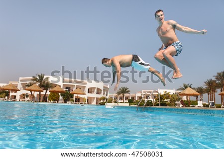 Two men jumping in swimming pool.  Low angle view from the swimming pool.