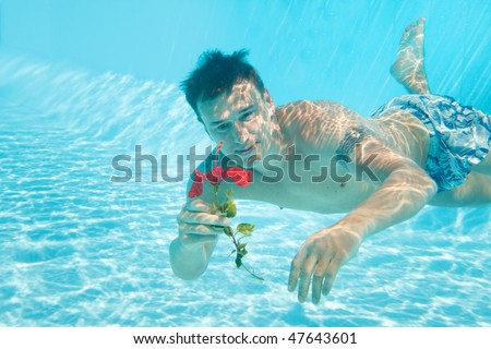 Man swimming with open eyes underwater in pool holding flower