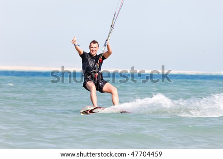 Kiteboarder enjoying surfing in blue water and showing thumbs up