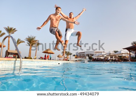 Two men jumping in swimming pool together.  Low angle view from the swimming pool.