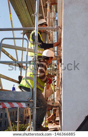 Two men standing on scafolding hight from ground and restoring the wall of old church in Europe