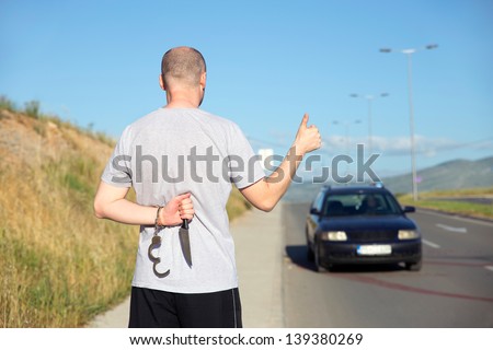 Hitchhiker. Young man hitchhiking on road - hiding a knife at his back