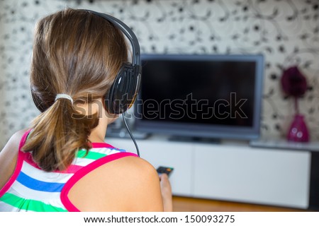Pretty girl listening to music with headphones  in the living room  and watching tv