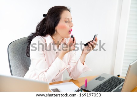 young business woman looking in the mirror and using lipstick in the office