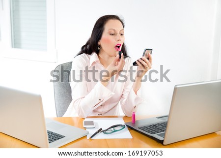 young business woman looking in the mirror and using lipstick in the office