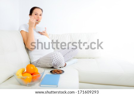 Beautiful pregnant woman eat cereals  on sofa at home