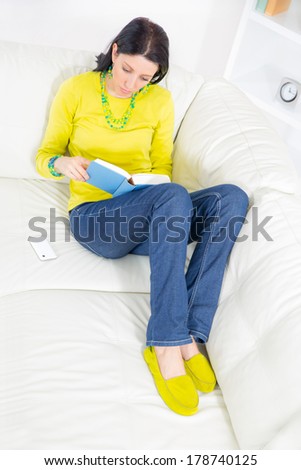 A young woman lying on her back on the sofa reading book