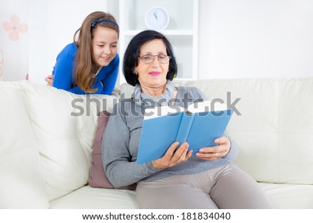 Grandmother and little girl reading a book happy together at home