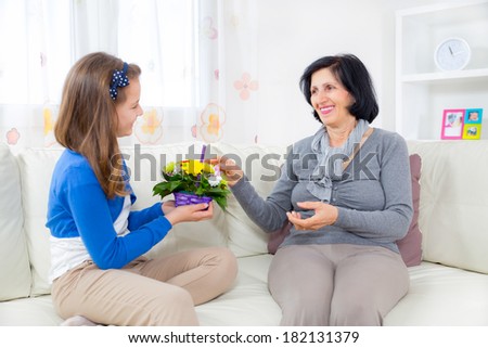 Cute girl giving a bunch of flowers to her grandmother sitting on the couch