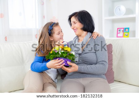 Cute girl giving a bunch of flowers to her grandmother sitting on the couch