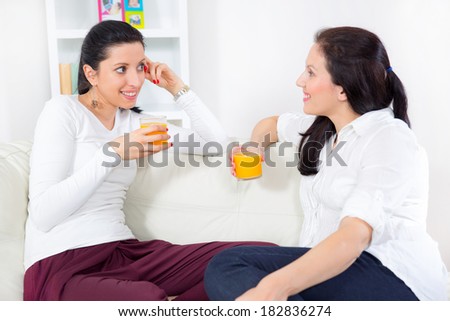 Two happy young female friends with juice conversing in the living room at home