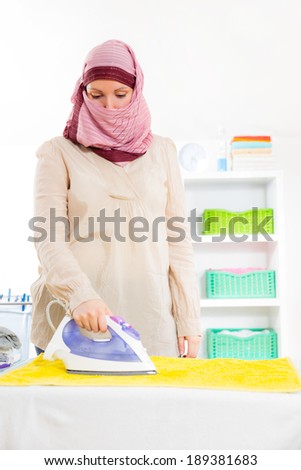Young muslim housewife standing at the ironing board ironing clothes