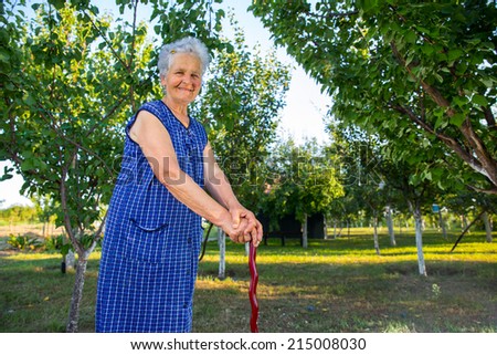 Elderly lady with stick walks through park