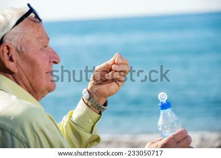 Older man drinking pills and looking at the sea