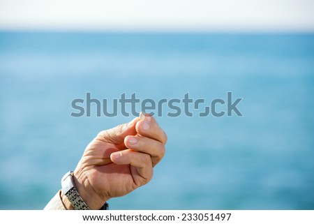 Elderly hand holding a pill, in the background you can see the sea