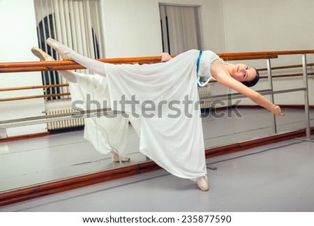 Beautiful classic ballet dancer in white tutu posing on one leg next to handle bar.