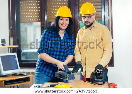 Home improvement - handy woman sanding wooden floor in workshop, handy man assisting, selective focus