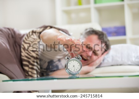 Man lying in bed turning off an alarm clock in the morning.