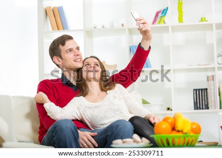 Smiling couple taking self portrait picture with telephone at home, selective focus