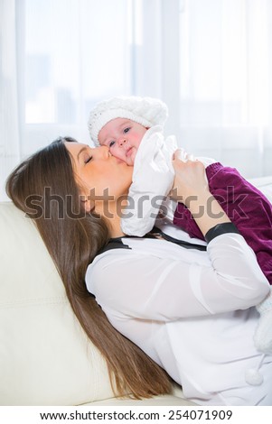Young woman holding her baby in her arms while sitting on a sofa in the living room