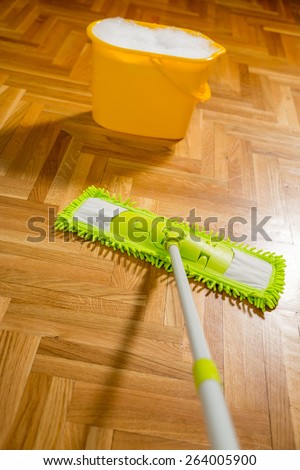 Cleaning the floor with a mop. Yellow bucket is filled with water and foam. Selective focus